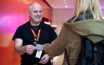 A photograph of a Visitor Engagement Assistant greeting a visitor at Tate Liverpool + RIBA North