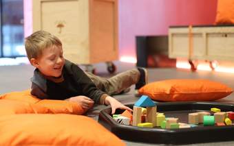 A photograph of a child laying down and playing with some building blocks.