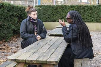 Two people having a conversation sitting at a picnic bench outdoors