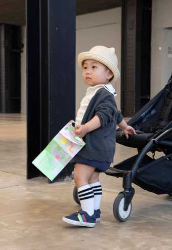 a toddler stands by their pram and holds an art resource called 'buggy walk'