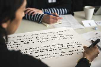 Two people sat opposite each other at a table writing notes