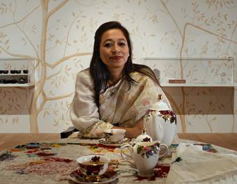 Artist Yasmin Jahan Nupur sitting at a table with an ornate tea set