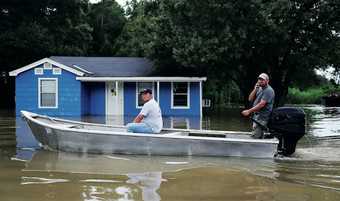 People navigate a flooded road by boat as they visit their neighborhood in Sorrento, Louisiana on 16 August 2016