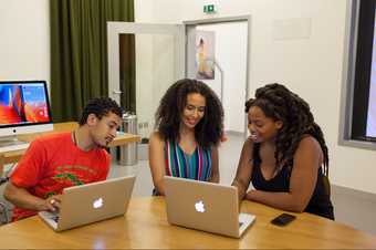 Photograph of three people seated around a table looking at laptops