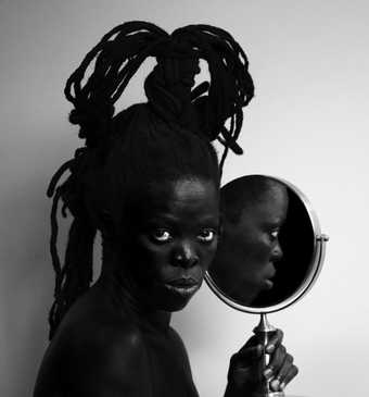 Black and white photo of the artist holding a mirror