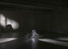 Dimly lit industrial room with concrete walls and a stack of metal that looks like rigging in the centre of the floor.