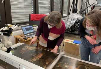 Two people look closely at a painting lain on a work table, with lab equipment around