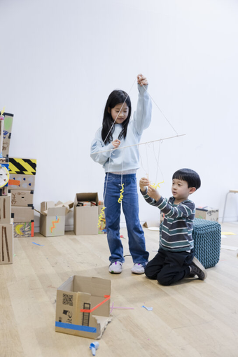 Two children make a triangular structure out of string