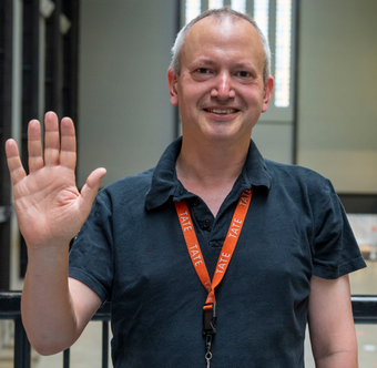 A visitor experience staff member smiles and waves at the camera